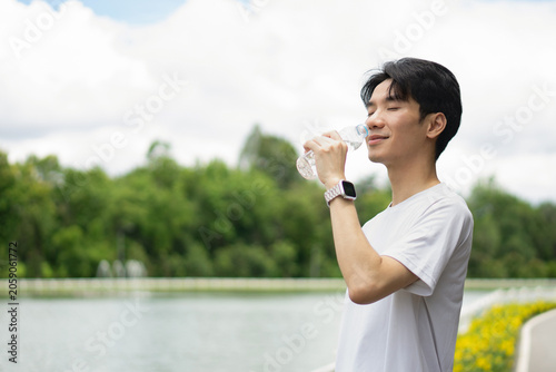 Fotografija A young Asian man, wearing a white T-shirt, closes his eyes, refreshed and smiling happily as he raises a bottle of water to quench his thirst
