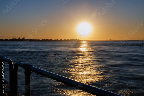 Sunset over water viewed past a waterfront railing