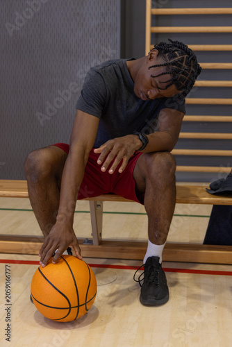 Basketball is resting on polished wooden court beside bench with folded towel and stall-bar