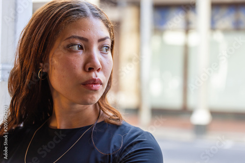 Female leaning on light column, gazing right on sidewalk with black top, chain necklace, copy space