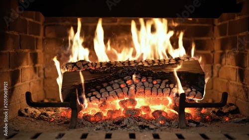 Flames dance around a burning log in a rustic fireplace, glowing embers and brick surround creating a warm and inviting atmosphere in a cozy indoor setting