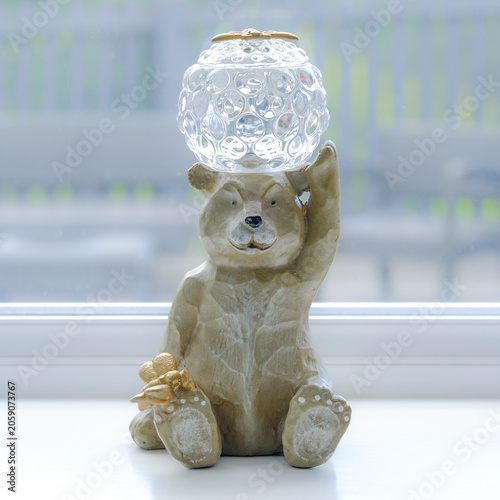 Bear holds crystal globe with gentle expression. Sitting by window, it appears calm and thoughtful. Soft lighting highlights its textured, earthy fur. Ideal for cozy, whimsical, or home decor themes