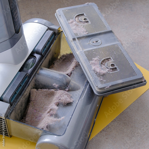 Vacuum cleaner shows collected dust and debris. Gray filters and housing reveal heavy use. Dusty interior hints at thorough cleaning efforts. Ideal for home cleaning or maintenance visuals