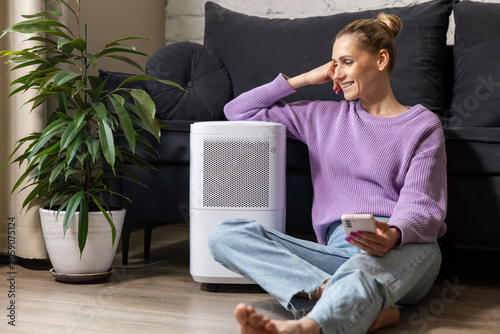 smiling woman sitting on the floor by air purifier at home. air quality and microclimate
