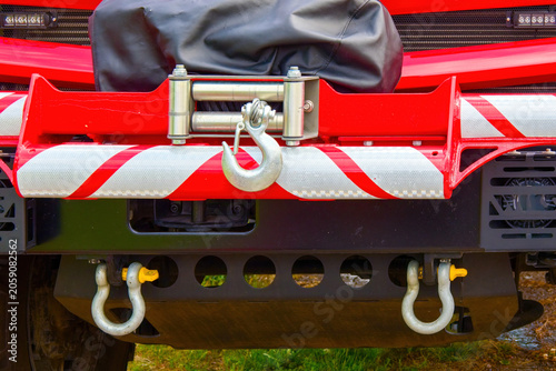 Foto Close-up of a heavy-duty electric winch with a steel hook mounted on the front bumper of a red rescue vehicle