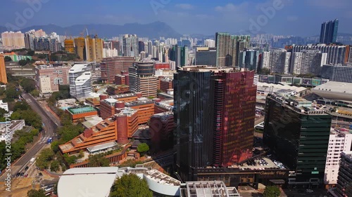 Vibrant urban highrise with glazed facade and colorful paneling in Hong Kong surrounding low rise blocks. Tree lined avenues in aerial angle highlighting density and mountain backdrop filmed at day