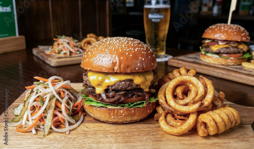 A large burger is served with a . curly fries and fresh salad. Two glasses of craft beer are next to the meal. are on the side. The setting is a restaurant with a warm atmosphere.