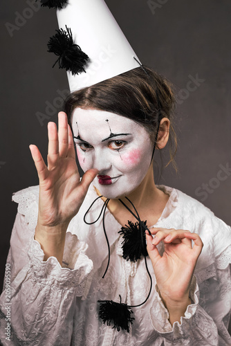 Playful woman in clown makeup gesturing thumb to nose holding hat string