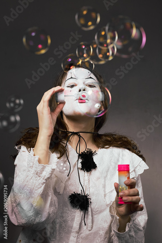 Woman in white clown makeup blowing soap bubbles from a pink bottle