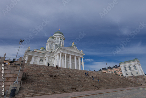 dramatic low-angle view of the iconic Helsinki Cathedral Helsingin tuomiokirkko rising above the massive stone steps of Senate Square. A few people are scattered across the stairs beneath a striking