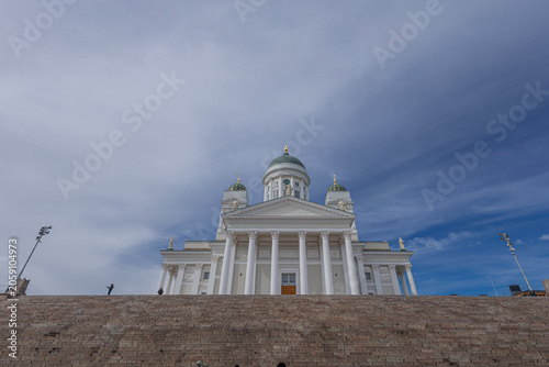 dramatic low-angle view of the iconic Helsinki Cathedral Helsingin tuomiokirkko rising above the massive stone steps of Senate Square. A few people are scattered across the stairs beneath a striking