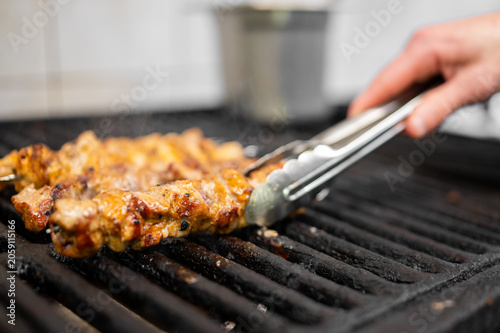Fotografie A close-up of chicken skewers being flipped with tongs on a hot outdoor grill