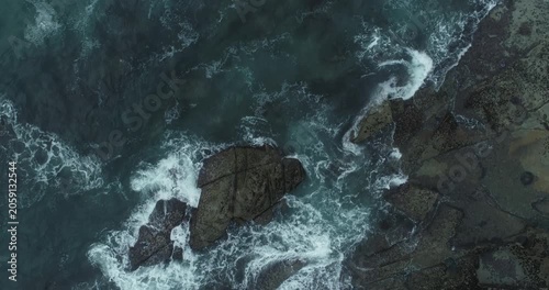 Dramatic drone photography of dark stones and white sea foam swirling in a turbulent ocean