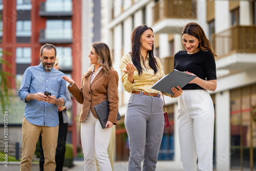 Business colleagues discussing a project outdoors in an urban office complex, smiling professionals collaborating