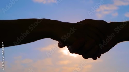 Close up view: silhouettes of man and woman are shaking hands against the sunrise or sunset sky - friendly handshake: sun lens flares. Greeting, agreement and friendship concept