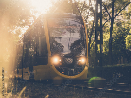 Modern tram moving on tracks in a city street during golden hour