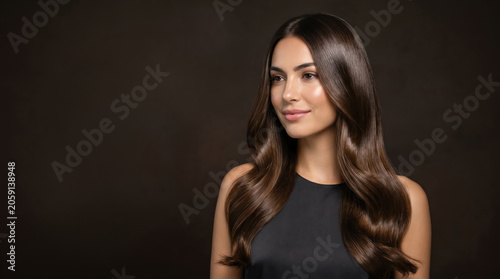 A woman stands in a dark space with long, wavy hair. She looks to the side with a calm expression. The lighting highlights her features. This is a simple indoor photoshoot
