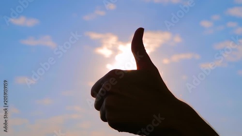 Close up shot: silhouette of woman is showing thumbs up hand gesture against the sunset, sunrise sky with sun lens flares. Approval, satisfaction and positive concept