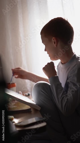 A teenager paints a paint-by-numbers picture on canvas with a brush. A boy dips a brush into paint and creates a creative drawing on a canvas. High quality FullHD footage