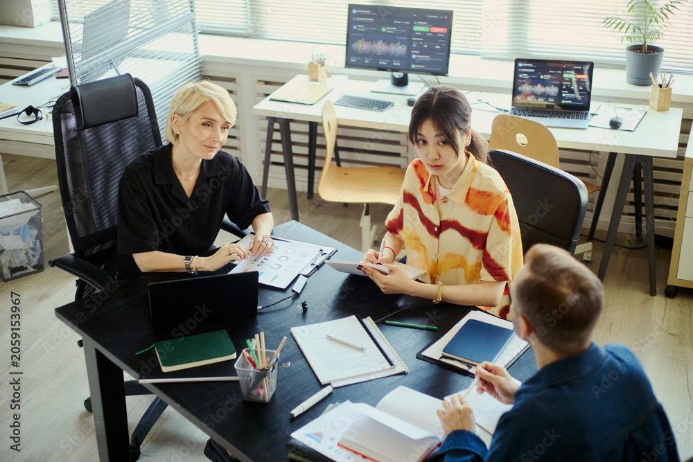 Fototapeta premium Diverse business team collaborating in office, reviewing reports and discussing strategy during meeting. Ideal for workplace teamwork, project management, corporate planning concepts