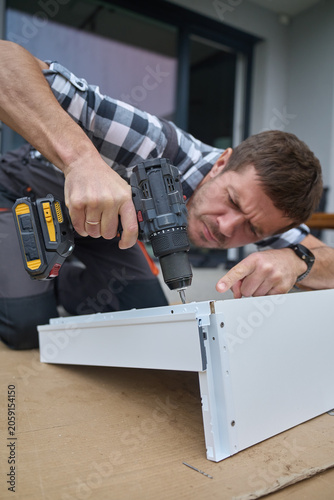 Man assembles furniture frame with cordless drill, aligns screw holes