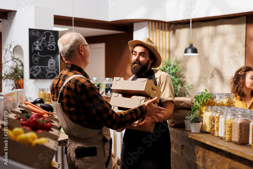 Фотография Vendor in zero waste supermarket refilling stock, receiving healthy locally grown vegetables from farmer while environmentally conscious supplier bringing organic non GMO food to merchant