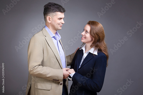 Loving Caucasian Mature Loving Couple Posing in Business Suits Together Embraced Over Gray Backround
