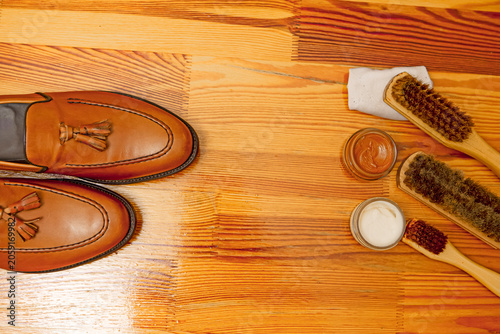 Tan Tassel Loafers Shoes Made of Calf Leather with Leather Sole Placed In Line With Shoe Cleaning Brushes On Wooden Table