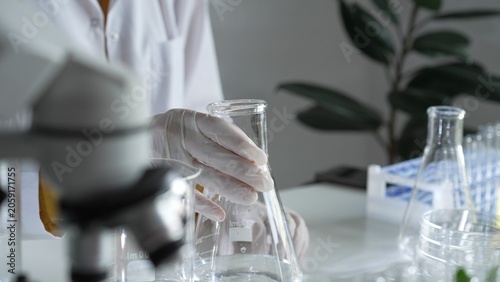 Cuadro en lienzo Unknown scientist wearing a lab coat and gloves is carefully pouring a liquid from a beaker into an Erlenmeyer flask, close up