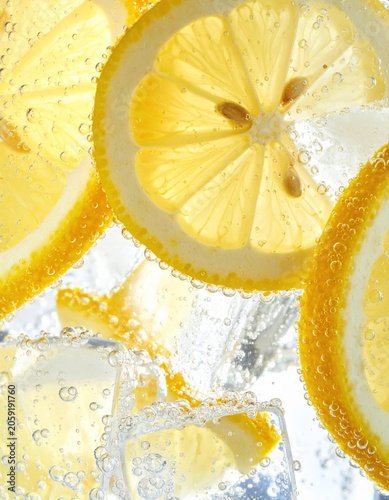 Fresh lemon slices submerged in fizzy sparkling water with clear ice cubes, creating refreshing bubbles and vibrant yellow textures for summer drink marketing.