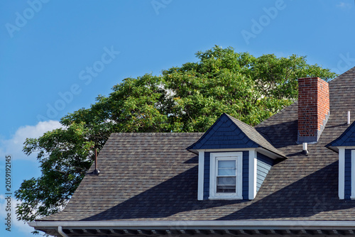Photos Traditional residential house roof with dark shingles and blue dormer window in