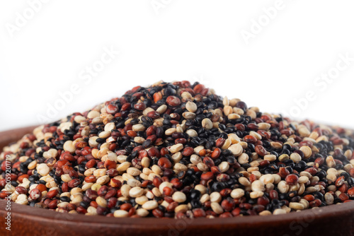 Mix of white, red, and black quinoa seeds in wooden bowl on white background