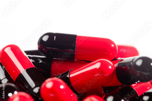 Heap of red and black hard capsule medicine on white background