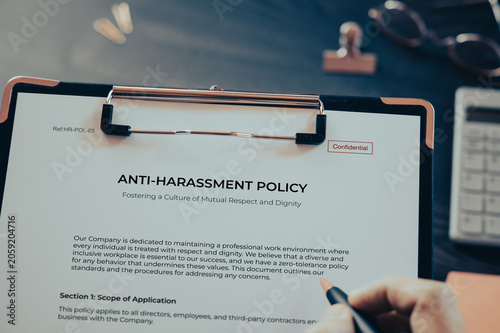 ANTI-HARASSMENT POLICY: Realistic clipboard-up placed on  with clips, calculator, pen. Contributor-created fictional business document for illustrative purposes.
