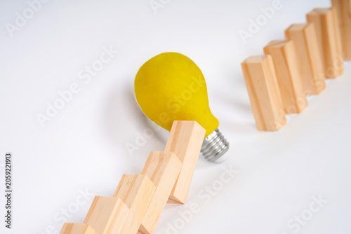 Fotografie A light bulb near fallen wooden blocks and a firm row of blocks, representing innovation, resilience and solutions for rebuilding ideas