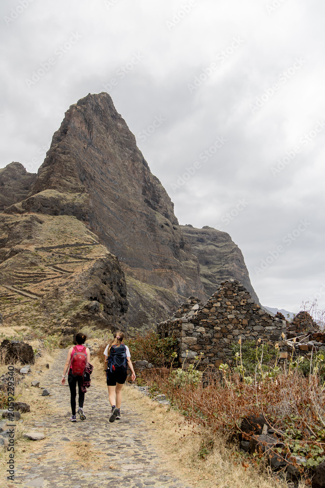 Obraz premium Two Hikers on Rocky Trail with Volcanic Peak Santo Antao