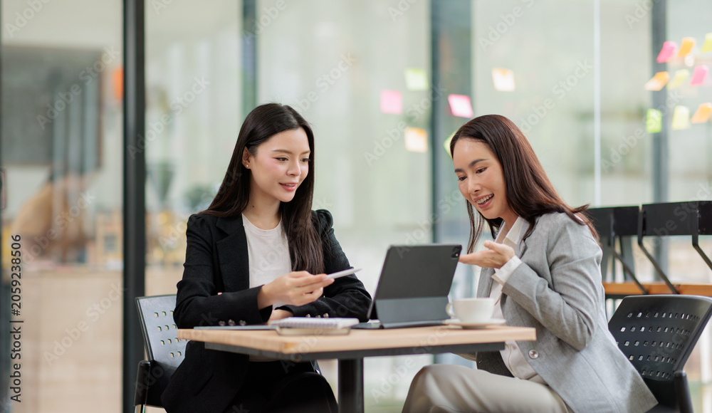 Obraz premium Young businesswomen collaborating on a project in a modern office, sharing ideas and making plans while using a digital tablet to discuss corporate strategies and achieve success