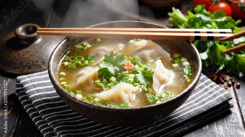 Hot dumpling soup in ceramic bowl with chopsticks.