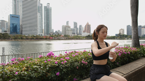 Fotografie Athletic Thai Woman Opening Water Bottle in Benjakitti Park Bangkok
