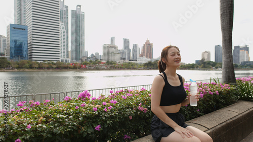 Obraz na plátně Athletic Thai Woman Resting with Water Bottle in Benjakitti Park Bangkok