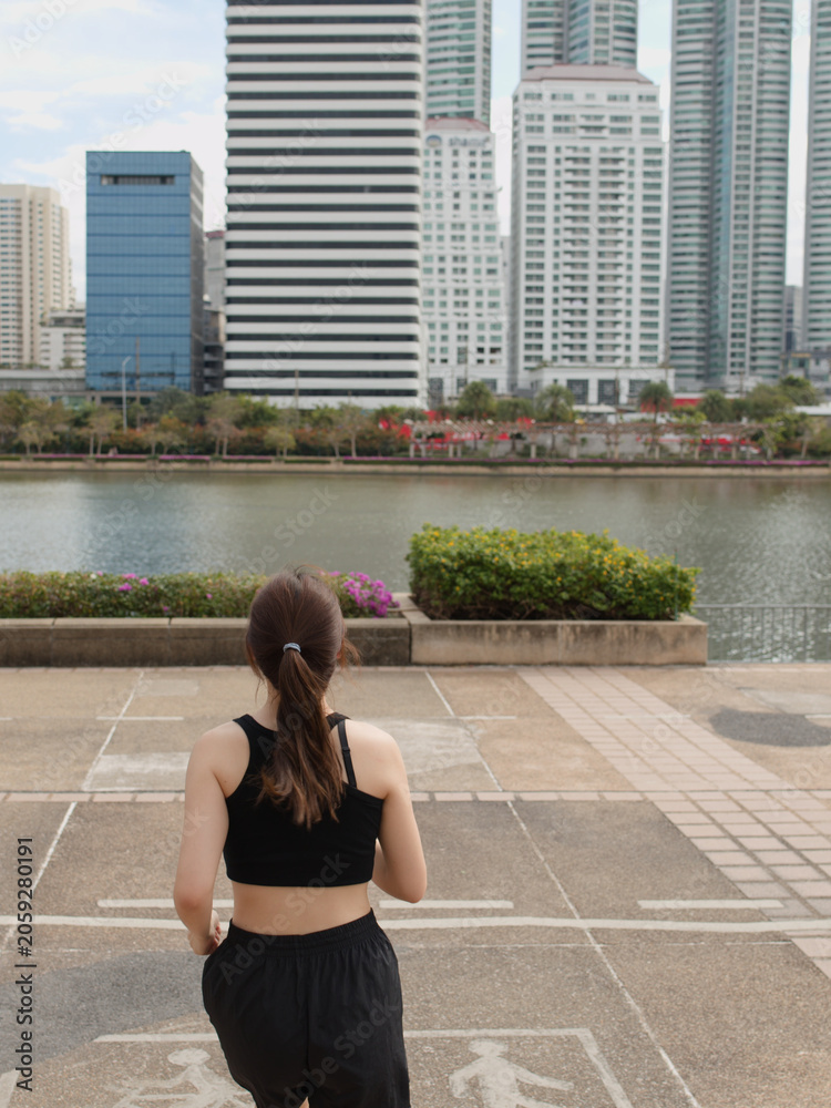 Fototapeta premium Rear view of young woman jogging towards city skyline in urban park