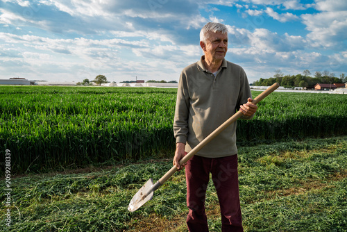 Senior farmer with shovel on his land outdoors , industrial field on sunny day 