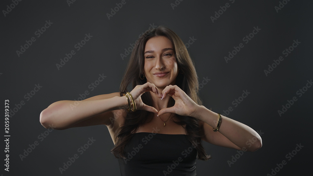 Fototapeta premium Young woman smiling at camera, making a heart shape with her hands