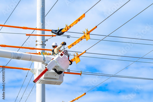 Utility lineman in bucket truck installing bright orange line guards and insulated blankets on high voltage overhead power lines