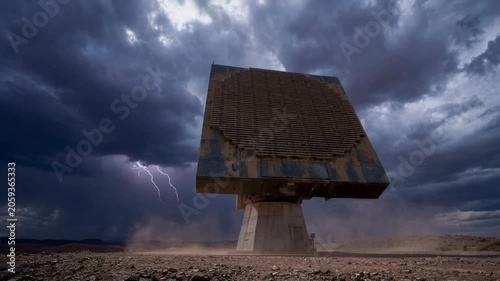 Storm clouds cover the desert. Satellite dish stands alone. Dust swirls around its base. Lightning flashes illuminate the scene. The sky is dark and threatening. Ideal for weather or science themes
