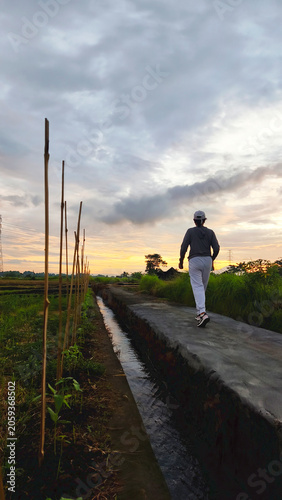 Woman walking on jogging track in the field at sunset sunrise. Healthy lifestyle concept. Walking in nature. Recharge.