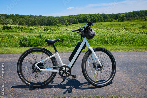 E-bike white step-through commuter electric bike sitting on a paved bicycle trail on a perfect summer day