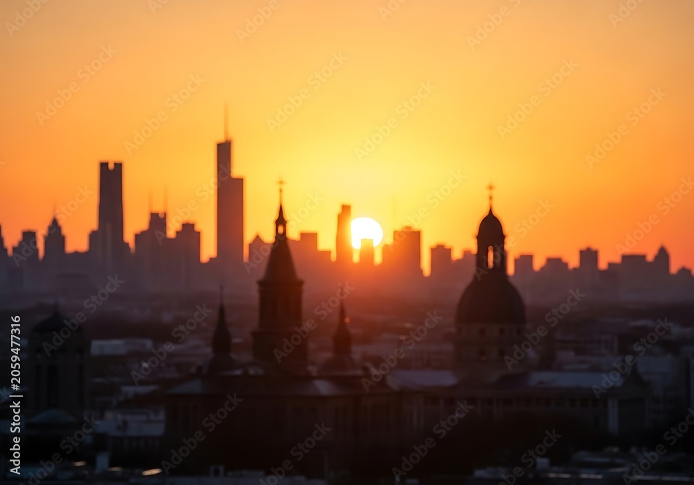 Obraz premium Dramatic silhouette of a city skyline against a vibrant orange and yellow sunset creating a peaceful urban landscape