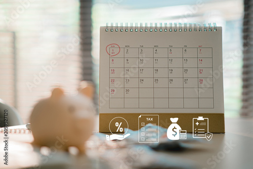 Desk calendar with financial tax payment icons and blurred piggy bank background