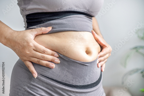 Close up of  woman in sportswear holding her fat belly, showing belly fat, love handles, or bloating after gaining weight, needing diet control or a weight loss program